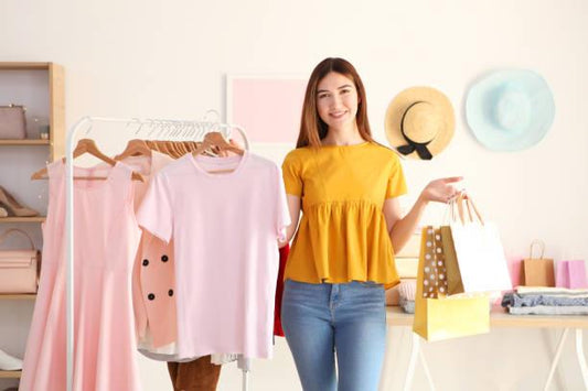 Young woman in a yellow top holding shopping bags and displaying women’s clothing on a rack, representing the best time to shop for affordable ladies' clothing